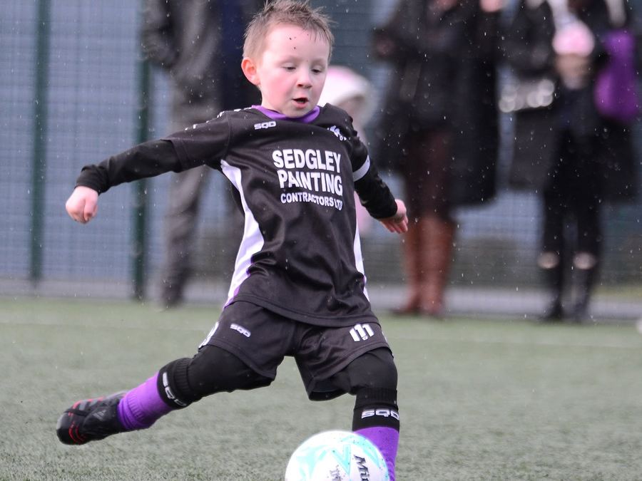 A young M11 player striking the ball in the rain in a Sedgley Painting Contractors kit